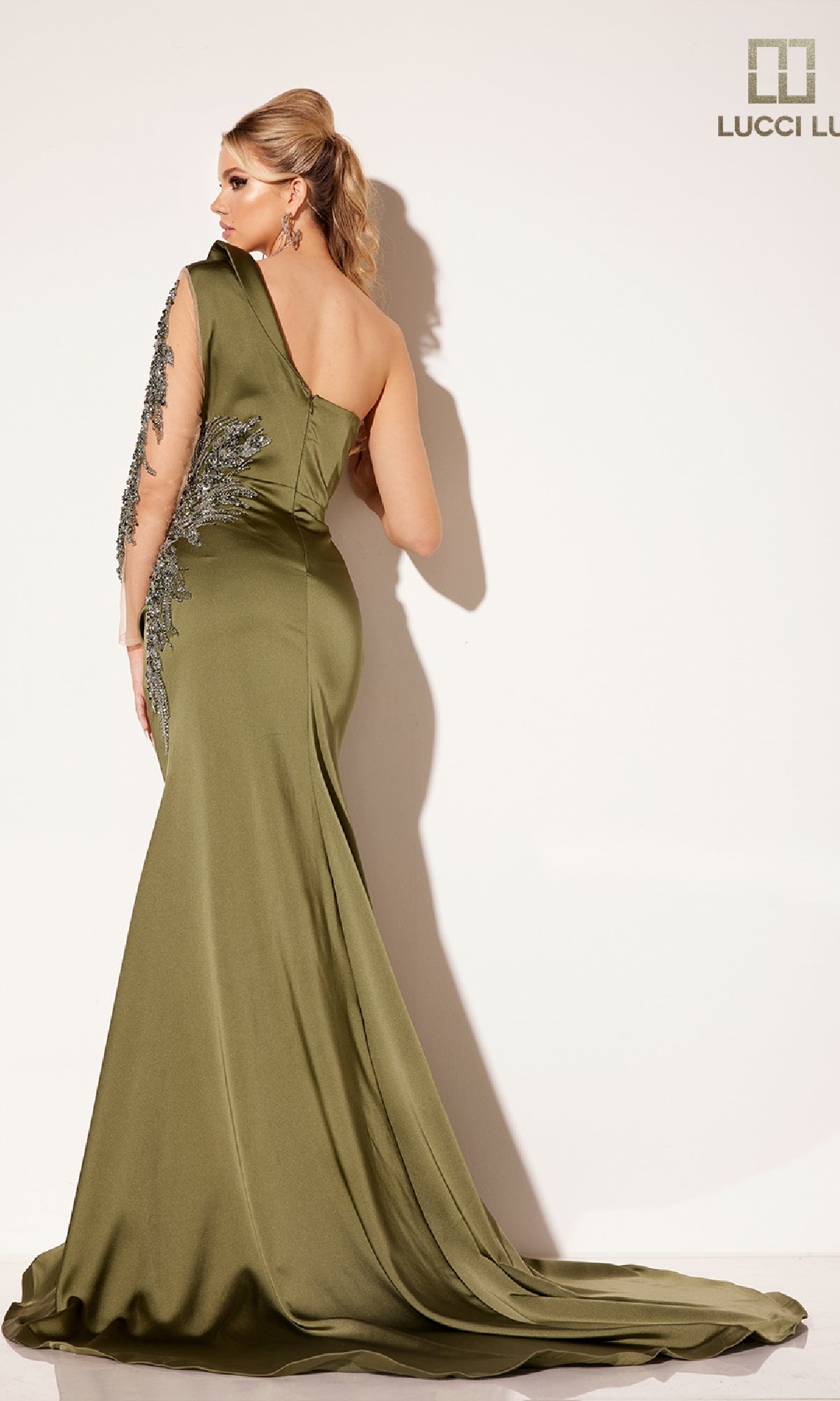 A woman models the Lucci Lu C8094 long formal dress, a fitted olive green one-shoulder gown with silver embellishments, posing with her back to the camera against a plain light background.